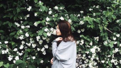 Woman with brown hair standing in front of floral garden wall